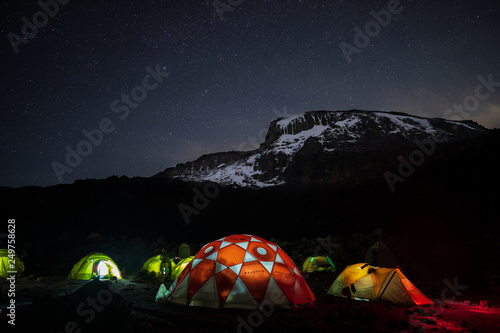 Lighted tents in the night in front of Mount Kilimanjaro