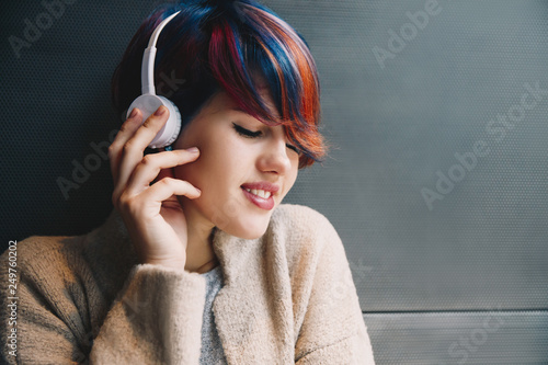 Technologies. Listening to music. Young woman with short colorful haircut in headphones is enjoying, her eyes are closed photo