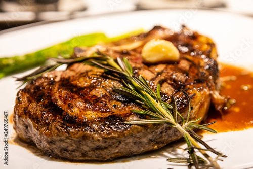 Fotografie A sprig of rosemary on a fresh roasted bone-in ribeye steak with garlic, gravy a