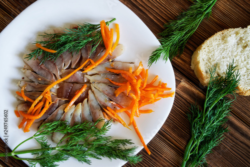 Slices of Scandinavian herring with spices, dill, pickled carrots and bread in a white plate photo