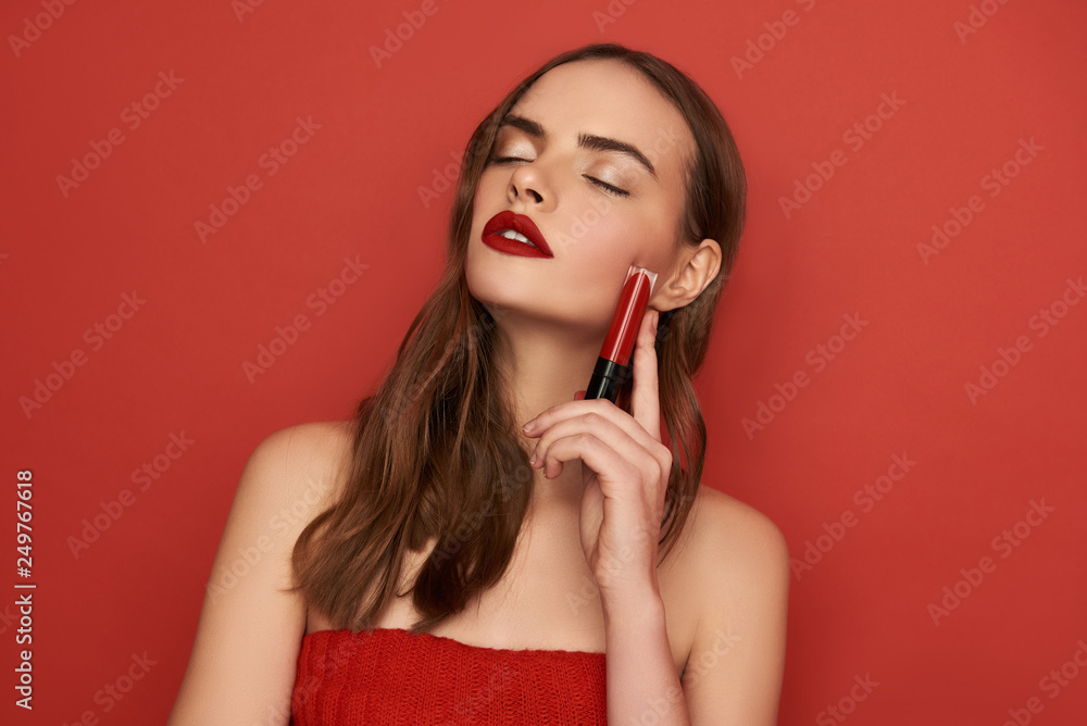Brunette Caucasian woman keeping cosmetics in arms on red background Brunette Caucasian woman keeping cosmetics in arms on red background