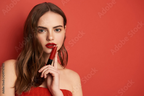 Close up portrait of charming girl holding bright lipstick on red background
