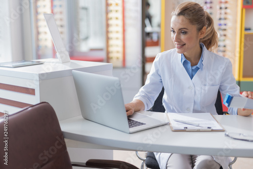 Billede på lærred Cheerful female ophthalmologist working at the optical store