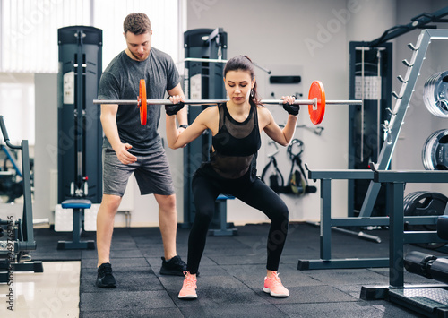 Young beautiful woman doing exercises with personal trainer. Beautiful girl squats under the supervision of the coach. © Vadim