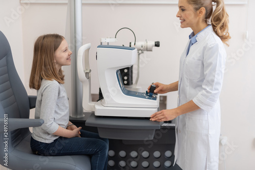 Female optometrist checking vision of little girl with autorefractor photo