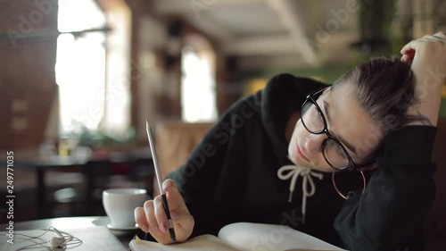 Girl sitting in cafe thinking while writing on notebook