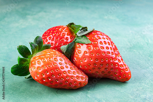PRIMER PLANO DE TRES FRESAS ROJAS SORBRE FONDO VERDE