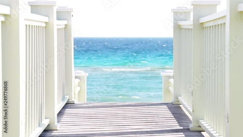View through wooden boardwalk stairs or steps and railing leading to beach on sunny day in Seaside, Florida panhandle town village with ocean sea in background