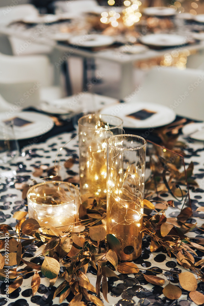 Dinner tableis decorated in black and gold. Garland in a glass flask. Wedding decorations
