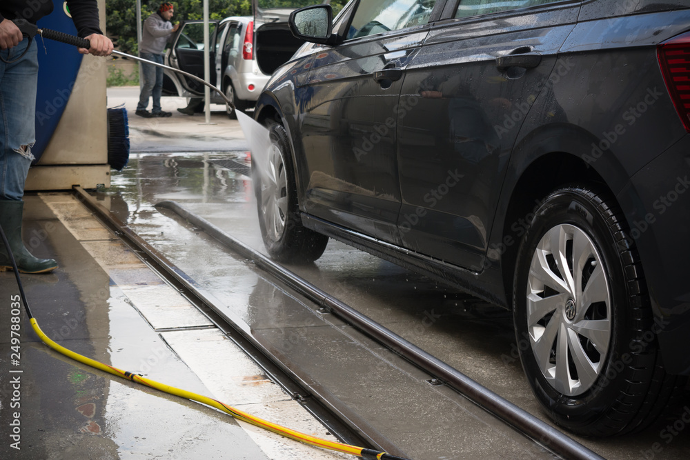 Man Using Water Pressure Machine to Wash a Car on Blurred Background