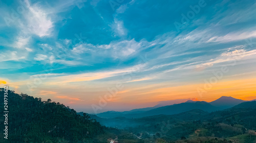 Beautiful nature landscape of mountain range with sunset sky and clouds. Rural village in mountain valley in Thailand. Scenery of mountain layer at dusk. Tropical forest. Natural background.