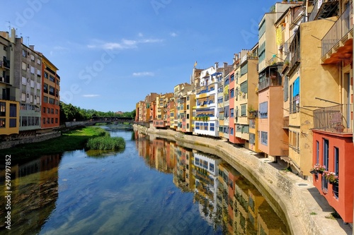 Colorful yellow and orange houses and Eiffel Bridge  Old fish stalls  reflected in water river Onyar  in Girona  Catalonia  Spain. Church of Sant Feliu at background.