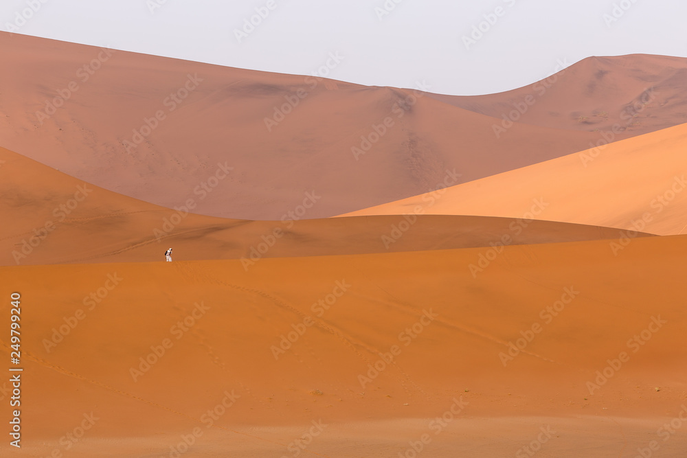 Tourist taking a photo dressed in white on orange sand dunes in Sossusvlei, Namibia