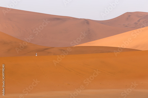 Tourist taking a photo dressed in white on orange sand dunes in Sossusvlei, Namibia