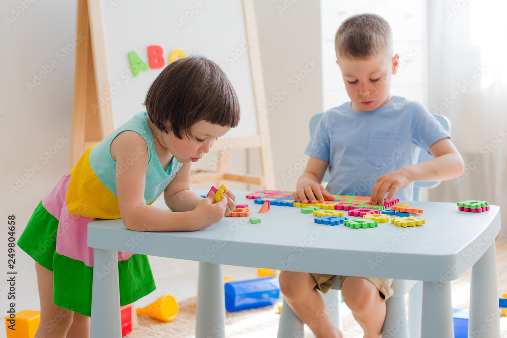 Fototapeta premium A boy and a girl collect a soft puzzle at the table. Brother and sister have fun playing together in the room.