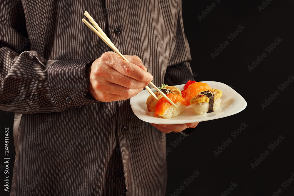 Hands of man in a black shirt using chopsticks take sushi from the plate on a black background