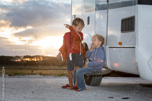 Two young boys engaged in conversation outside their motor home at sunset.