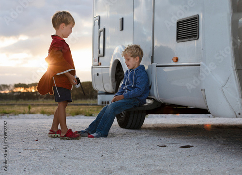 Two young boys engaged in conversation outside their motor home at sunset.