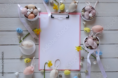 Easter Flat lay. Spring Easter Mockup.Decorative eggs  blank notepad yellow daffodils flowers on gray wooden board background.