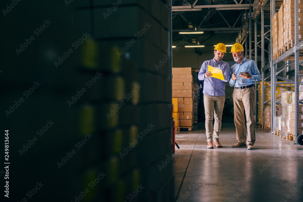 Obraz premium Two businessmen with helmets on heads discussing about shipping cargo. Storage interior.