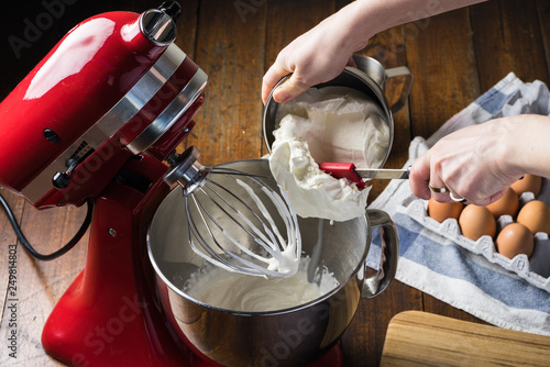putting cheese cream in bowl of standing red kitchen aid mixer with cream on whisk. on wooden floor