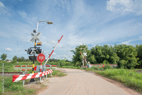 Railroad Barrier,traffic signs and Railroad tracks stretches. green trees with the blue sky as the background. 