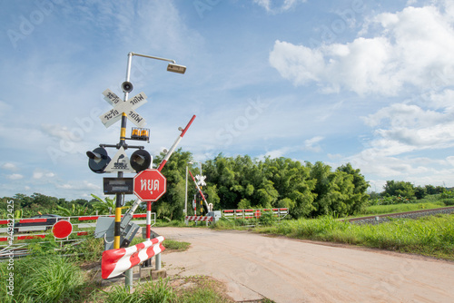 Railroad Barrier,traffic signs and Railroad tracks stretches. green trees with the blue sky as the background. 