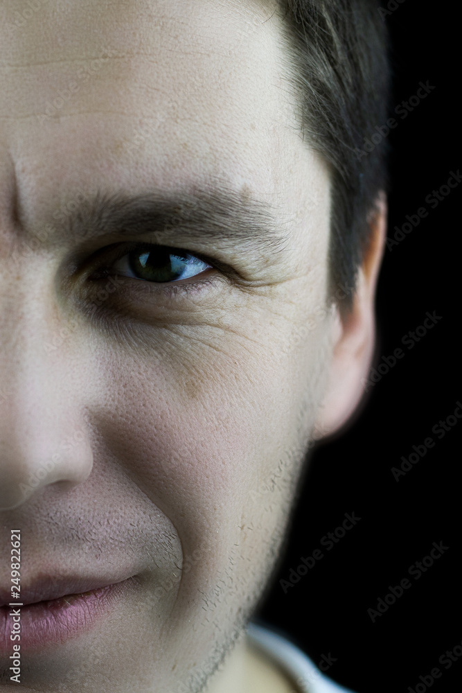 Left half of the face of a confident man close up. Fragment of a male face close-up on a black background. Studio photo of a male face with skin texture, wrinkled eyes. Left half of the face of a confident man close up. Fragment of a male face close-up on a black background. Studio photo of a male face with skin texture, wrinkled eyes.