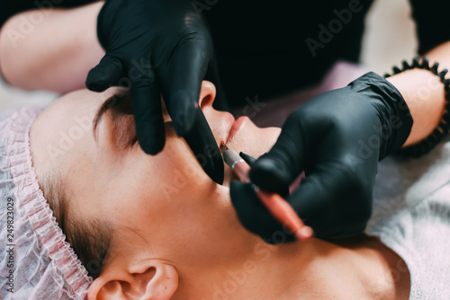 Permanent make-up for red Lips of beautiful woman in beauty salon. Closeup beautician doing tattooing Lips.