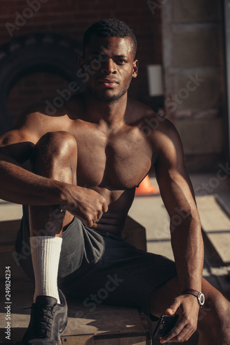 Handsome African American bodybuilder man, with naked muscular torso posing against red brick wall.