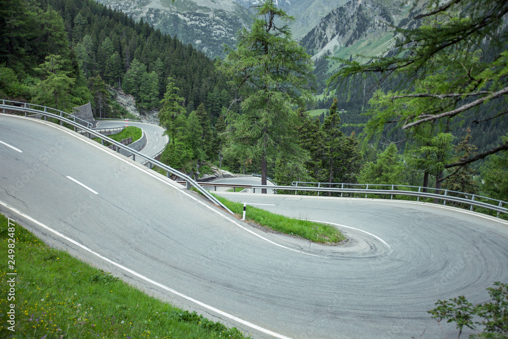 Road curves at Maloja Pass in Switzerland. Sunny day with green vegetation and a few serpentines.
