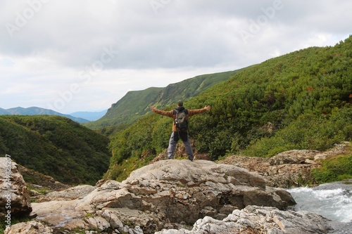 Man stands with open arms on the stone by mountain Tahkoloch river in the caldera of the extinct Vachkazhets volcano on  the Kamchatka Peninsula, Russia. photo