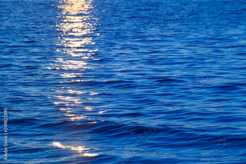 Sunset at Sea Detail / Reflecting yellow sunlight at sunset on blue water surface background (copy space)