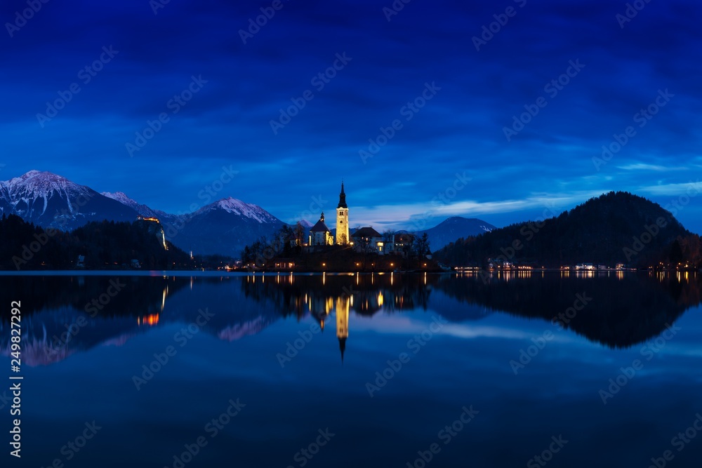 Fototapeta premium Beautiful view of famous Bled Island (Blejski otok) at scenic Lake Bled with Bled Castle (Blejski grad) and Julian Alps in the background in golden morning light at sunrise in summer, Slovenia 