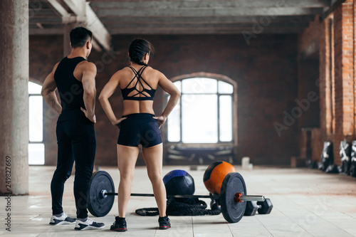 strong man and woman with hand on hip looking at sport equipment . back view photo. copy space