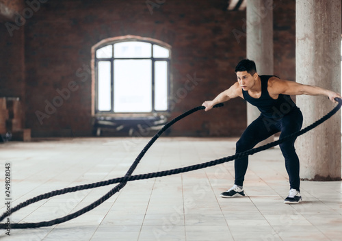 modern workout tool. awesome athlete develops muscles and cardio with battling rope. side view full length photo. copy space