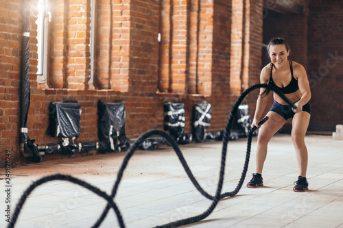awesome female athlete develops muscles and cardio with battling rope in the sport session . side view full length photo. motivation