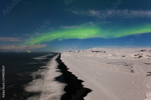 Aurora borealis, Iceland. Green northern lights. Starry sky with polar lights. Night winter landscape with aurora, sea with sky reflection and snowy mountains and black beach. Nature background 