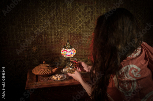 Glass of black tea in woman`s hand at Low light lounge interior with carpet. Eastern tea concept. Eastern snacks on vintage wooden surface. photo