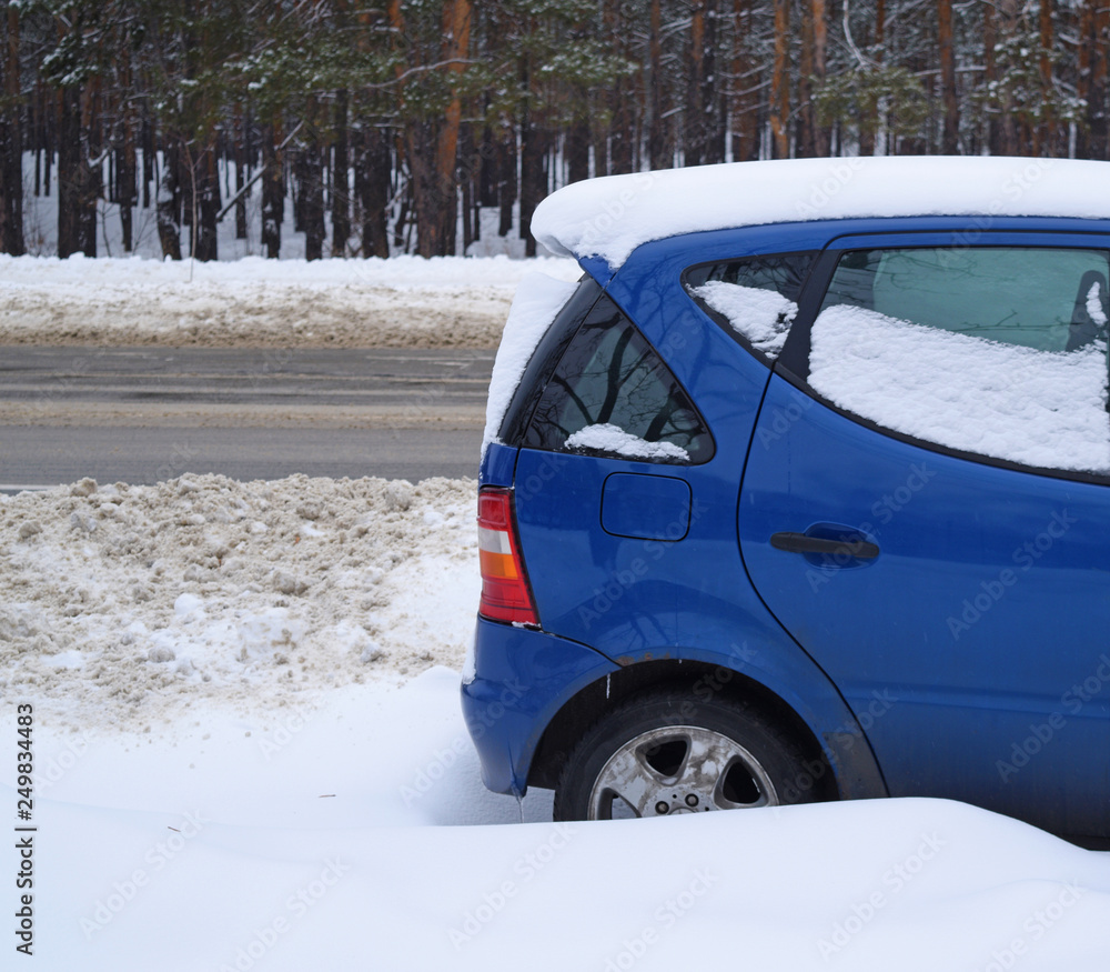 Blue car in the snow near the road and forest.