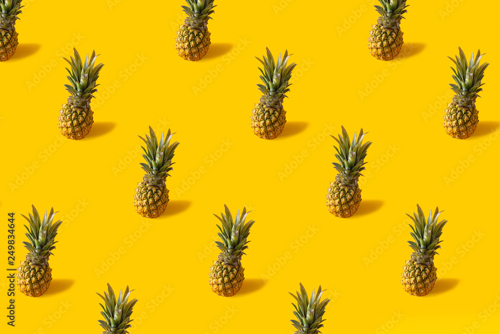 Fototapeta premium Summer colorful fruit minimal pattern of fresh pineapples on yellow background with shadow