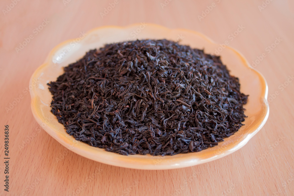 Black tea in a saucer on the table. Tea leaves, crushed, processed and ready to brew. Black tea in a saucer on the table. Tea leaves, crushed, processed and ready to brew.