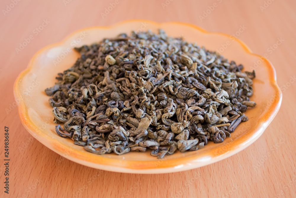 Green tea in a saucer on the table. Tea leaves, crushed, processed and ready to brew. Green tea in a saucer on the table. Tea leaves, crushed, processed and ready to brew.
