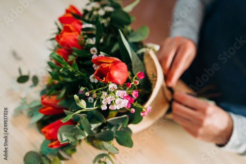 Woman florist makes a orange tulips bouquet on wooden table