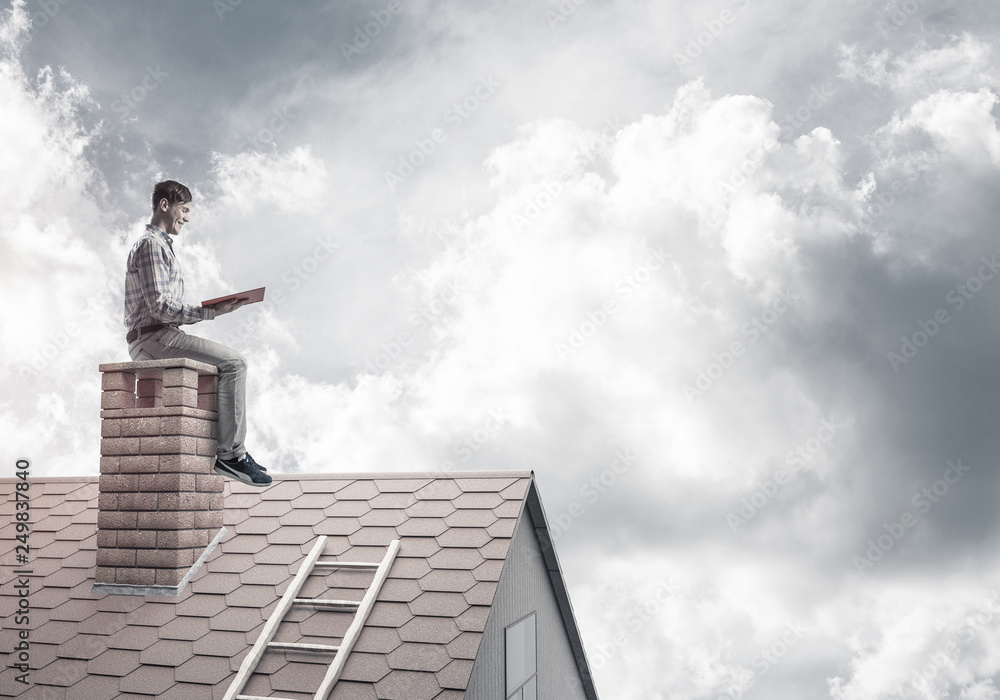 Handsome man on brick roof against cloud scape reading book Handsome man on brick roof against cloud scape reading book