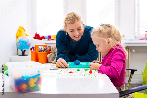 Toddler girl in child occupational therapy session doing sensory playful exercises with her therapist. photo