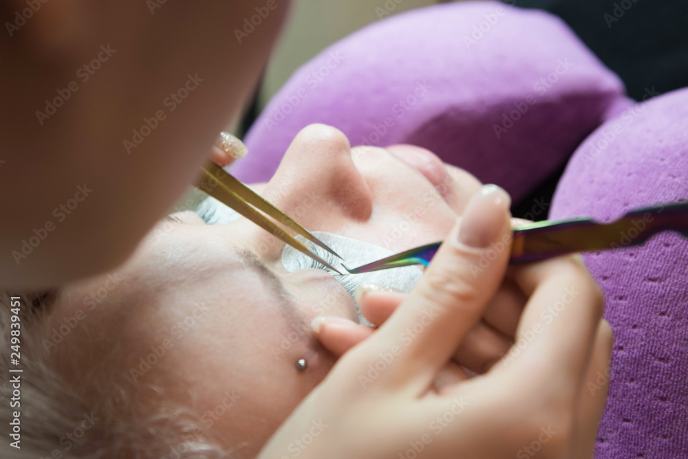 Beauty and fashion concept - Eye lash extension procedure. Young beautiful woman eye with long false eyelashes. Close up macro shot of fashion eyes in beauty salon. Beauty and fashion concept - Eye lash extension procedure. Young beautiful woman eye with long false eyelashes. Close up macro shot of fashion eyes in beauty salon.