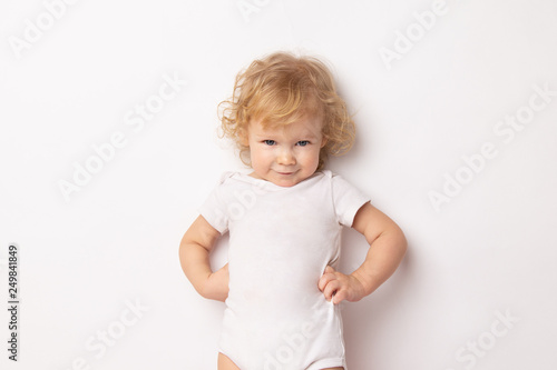 Caucasian curly baby girl in a white T-shirt on a white background hands holding a waist. child hands in hips