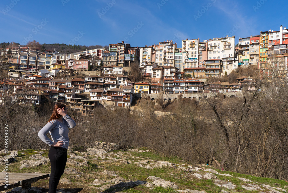 Young red head girl in a park outside of the town of Veliko Tarnovo in Bulgaria with old houses and trees in a sunny day