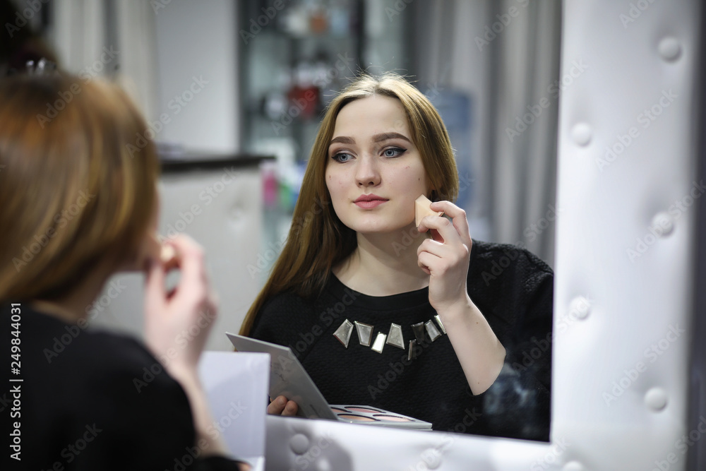 A young girl does make-up in a beauty salon. The girl in front of the mirror is making up. Beauty saloon. A young girl does make-up in a beauty salon. The girl in front of the mirror is making up. Beauty saloon.
